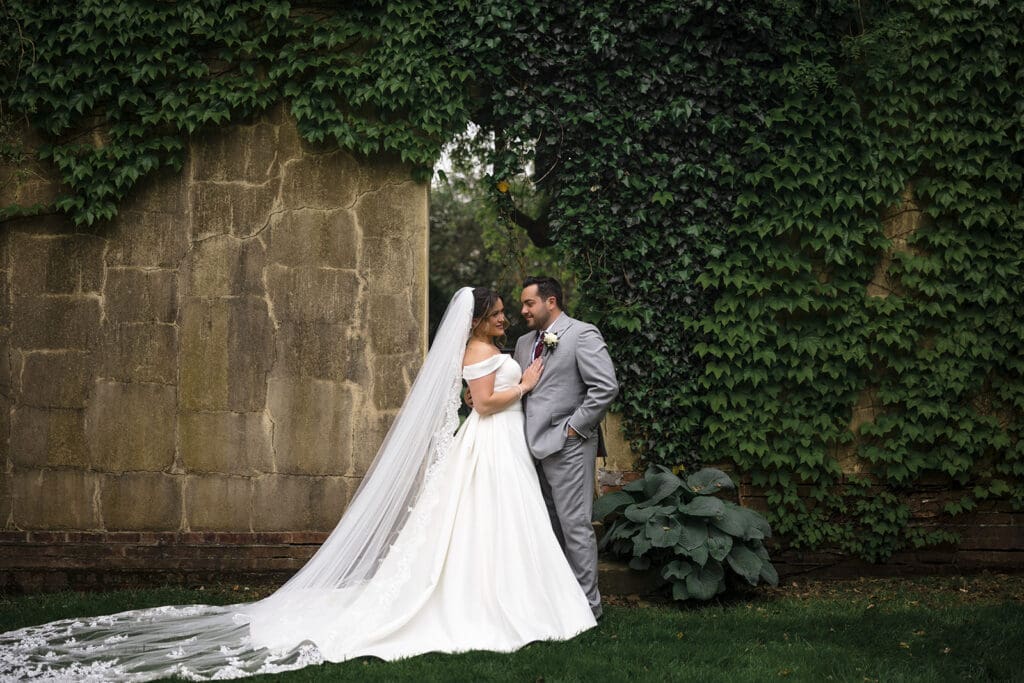 Bride and groom photo in surrounded by a stone wall covered in vines