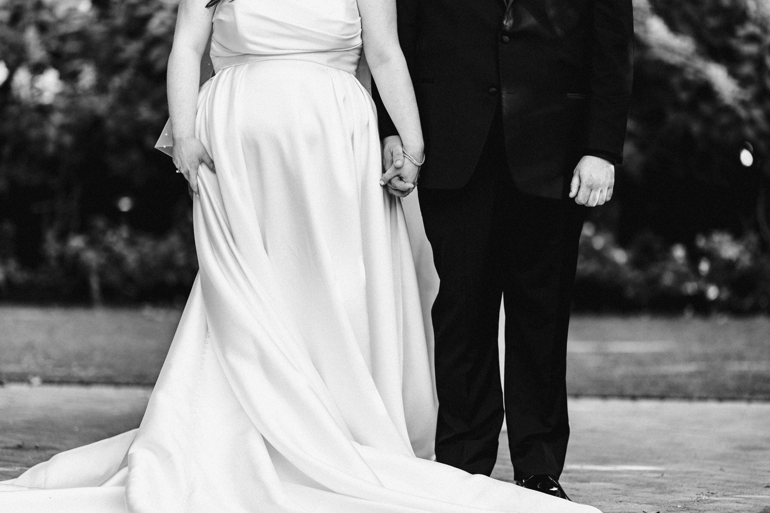 B&W photo from the chest down of a bride and groom holding hands during their wedding ceremony at Larkfield